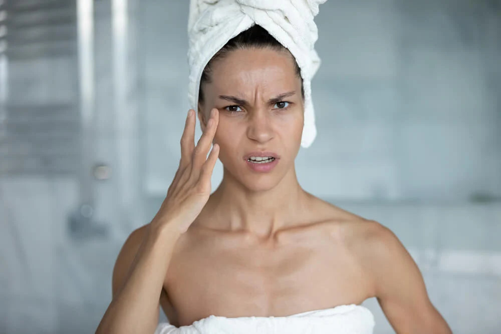 Woman checking her skin in the mirror for signs of common skincare mistakes like over-exfoliation