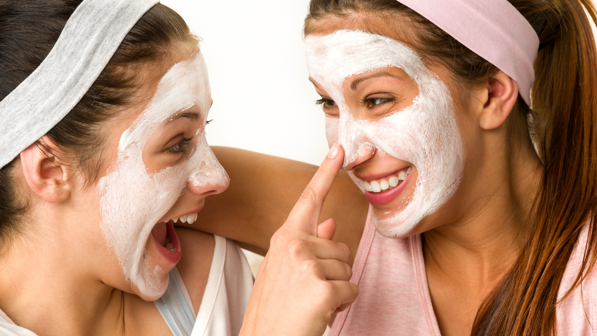 Two teenage girls wearing white face masks and laughing together