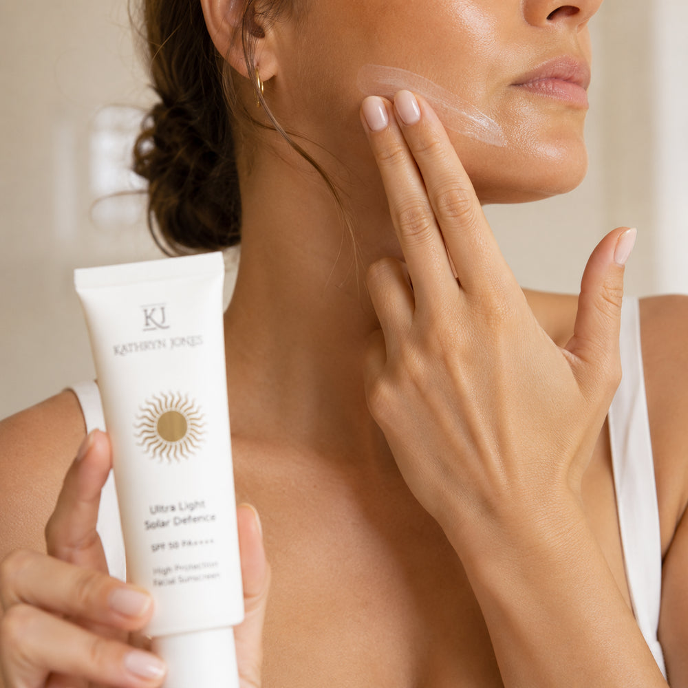 Woman applying KJ Serums Ultra Light Solar Defence SPF 50 PA++++ sunscreen to her face, showing zero white cast and smooth absorption